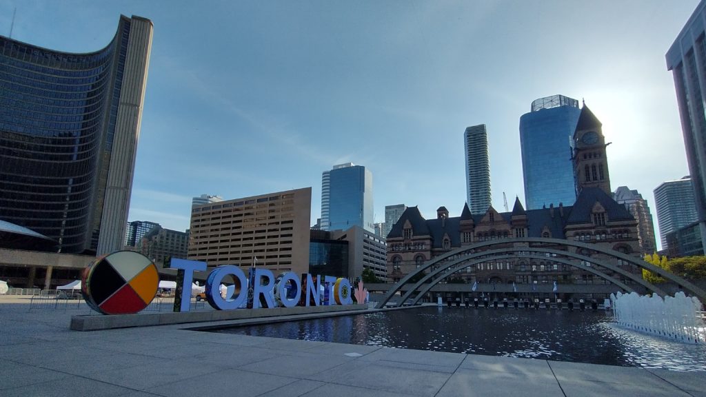 Toronto sign at Nathan Phillips Square with City Hall and Old City Hall on a sunny day