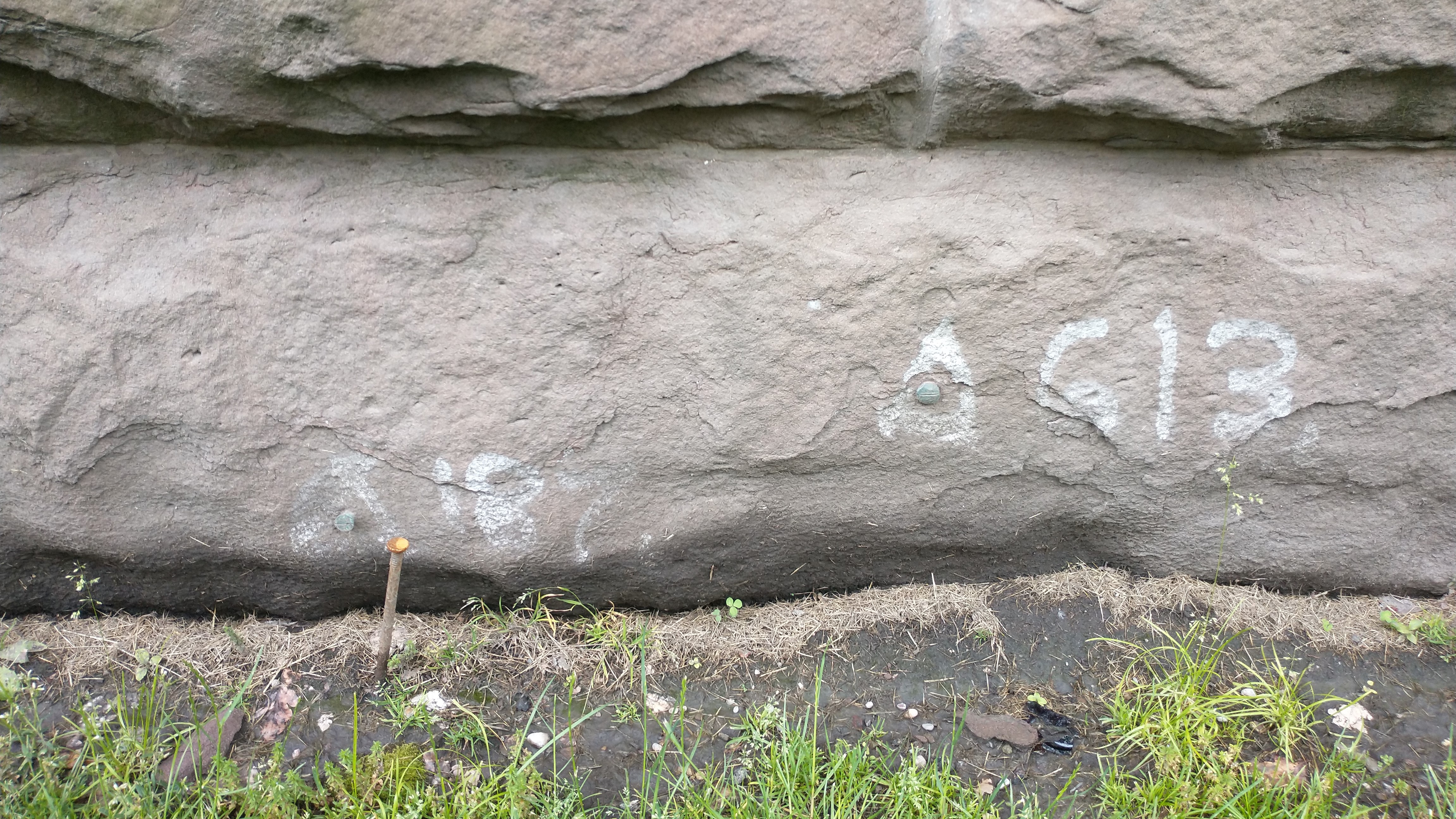 Two survey monument bolts in a stone wall with triangles around them and identifying numbers