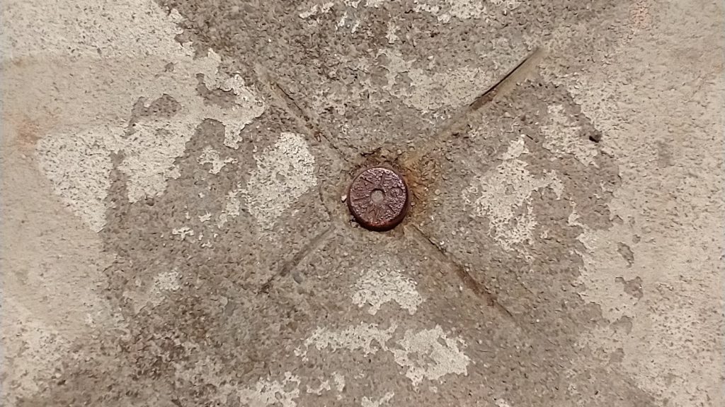 A cross marked in concrete as a survey monument with a nail in the middle with the letters MAG on its head