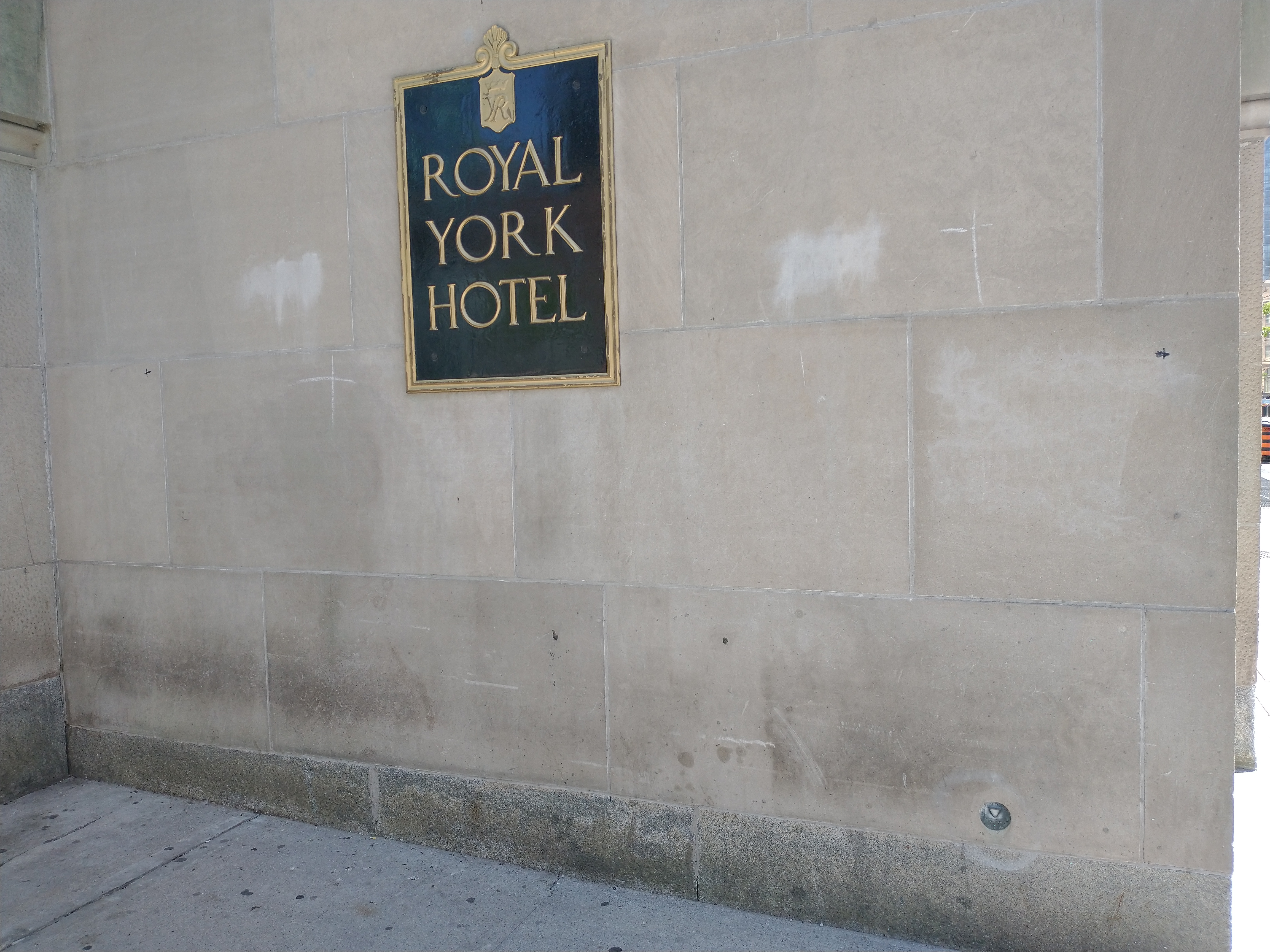 Stone wall with a sign reading Royal York Hotel at the top and a small bronze survey monument at the bottom right