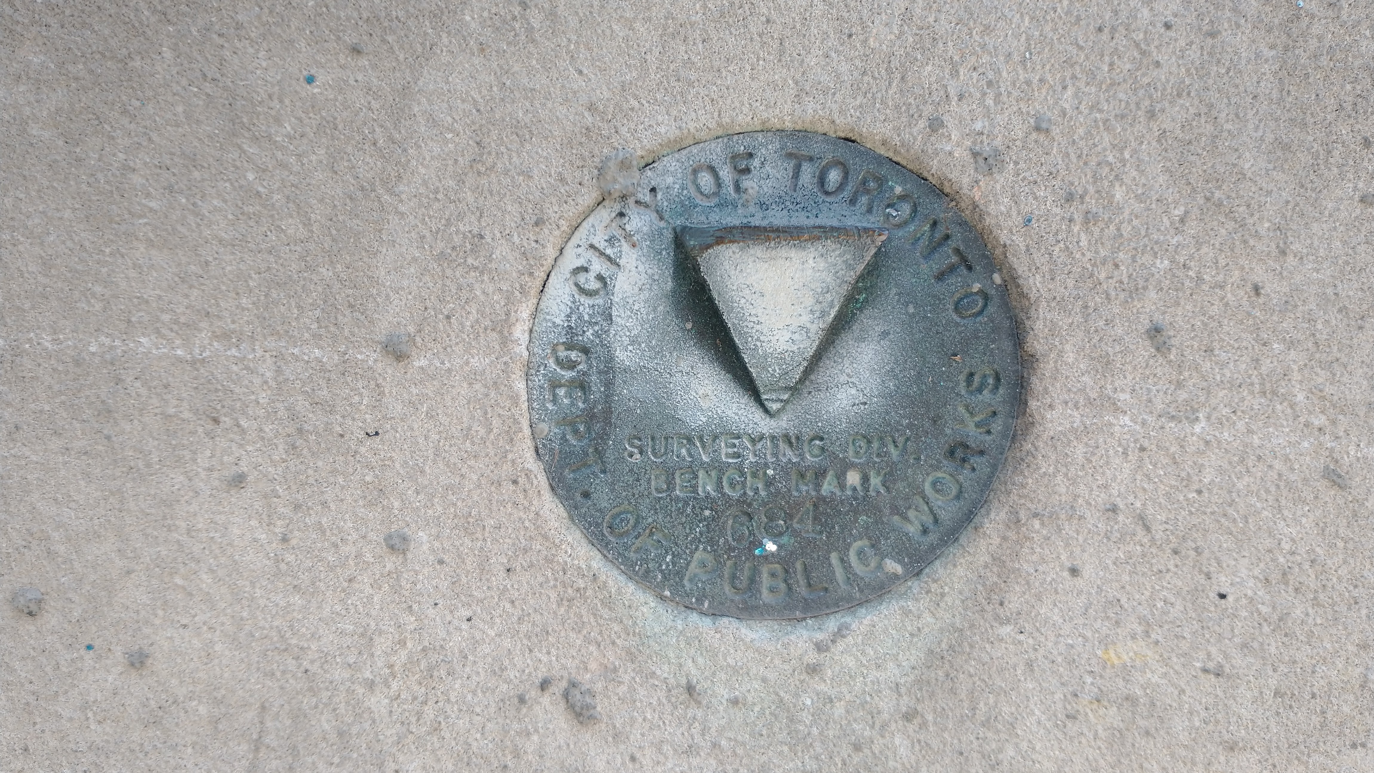 Bronze survey monument disc in stone wall with the words City of Toronto Dept. of Public Works Surveying Div. Benchmark